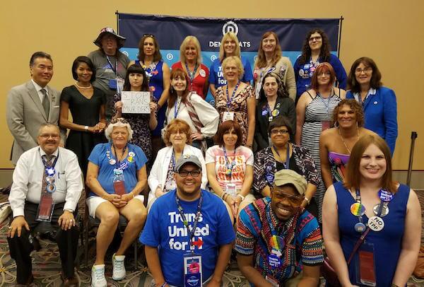 During a meeting of the convention’s LGBT caucus, out gay US Representative Mark Takano (at l. in third row) appears with 20 of the 28 trans delegates to the convention, including: (front) Lou Weaver, Merrick Moses, and Anita Green; (second row) Diego Miguel Sanchez, Joanne Carroll, Babs Siperstein, Melissa Sklarz, Marisa Richmond, and an unidentified non-delegate; (third row) Sharron L. Cooks, Mia Satya, (non-delegate) Elizabeth Coffey Williams, Jeanne Smith, Danielle Jessica Pellett, April Spilker, and Mara Keisling; and (fourth row) Wendy Ella May, Tiffany Woods, Mara Glubka, Kimi Cole, Sophia Jean Hawes-Tingey, and Monica Paige DePaul. FACEBOOK.COM/MELISSA.SKLARZ 